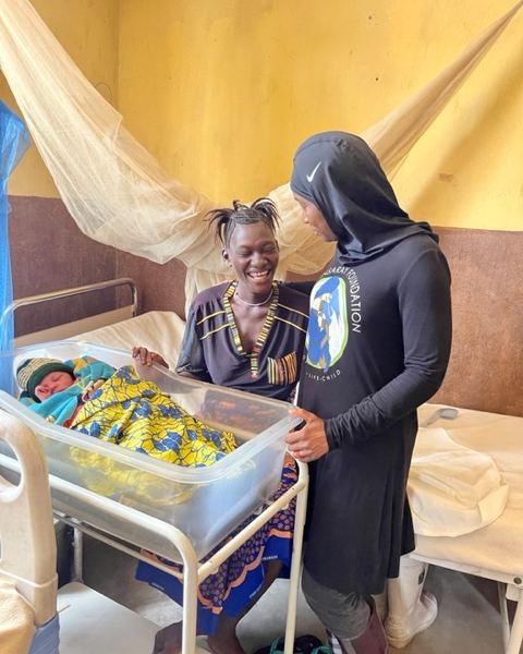 A TMF team member beside a mother and her newborn in a hospital cot