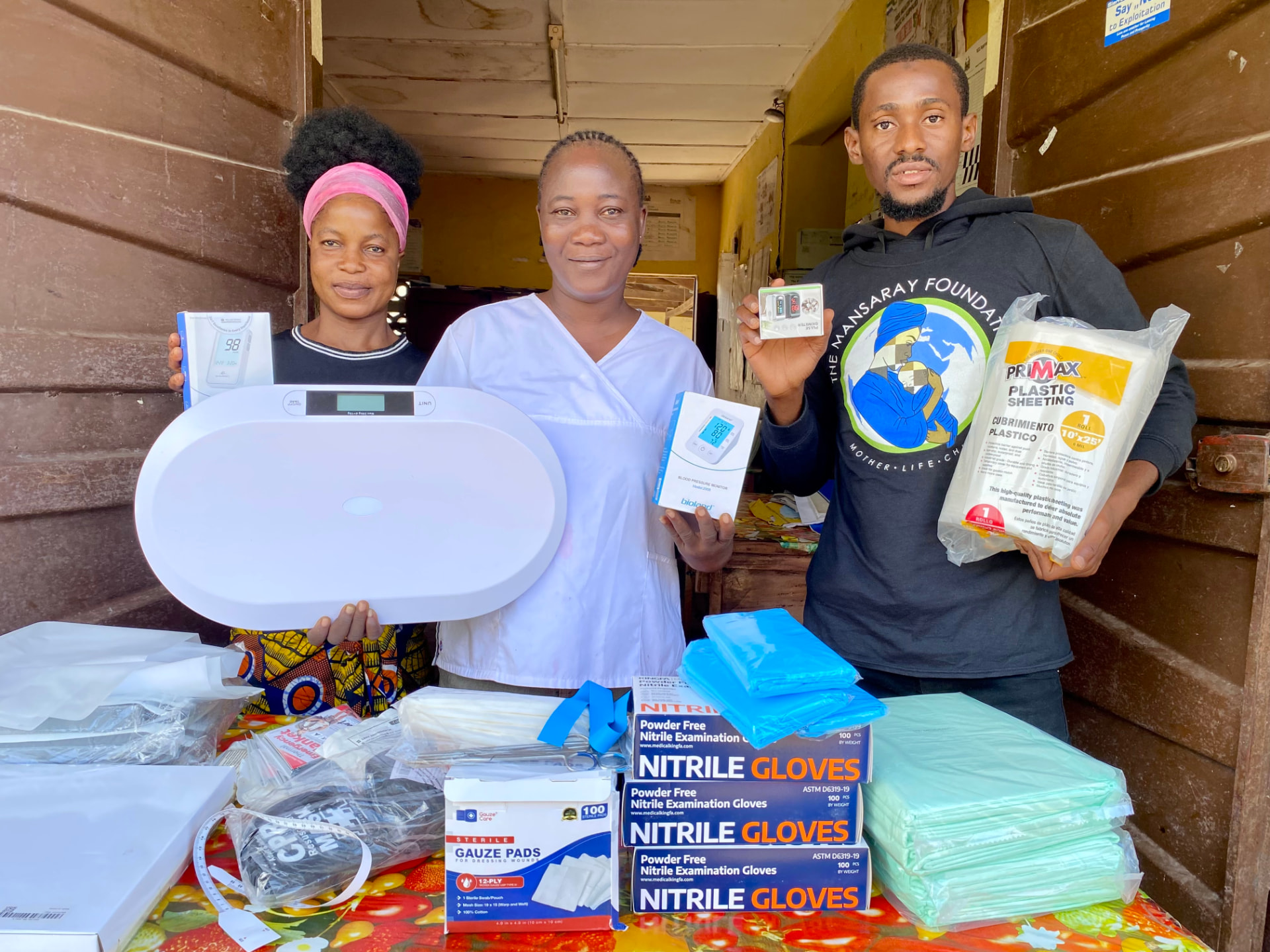 Three people presenting medical supplies and equipment outside a health facility.