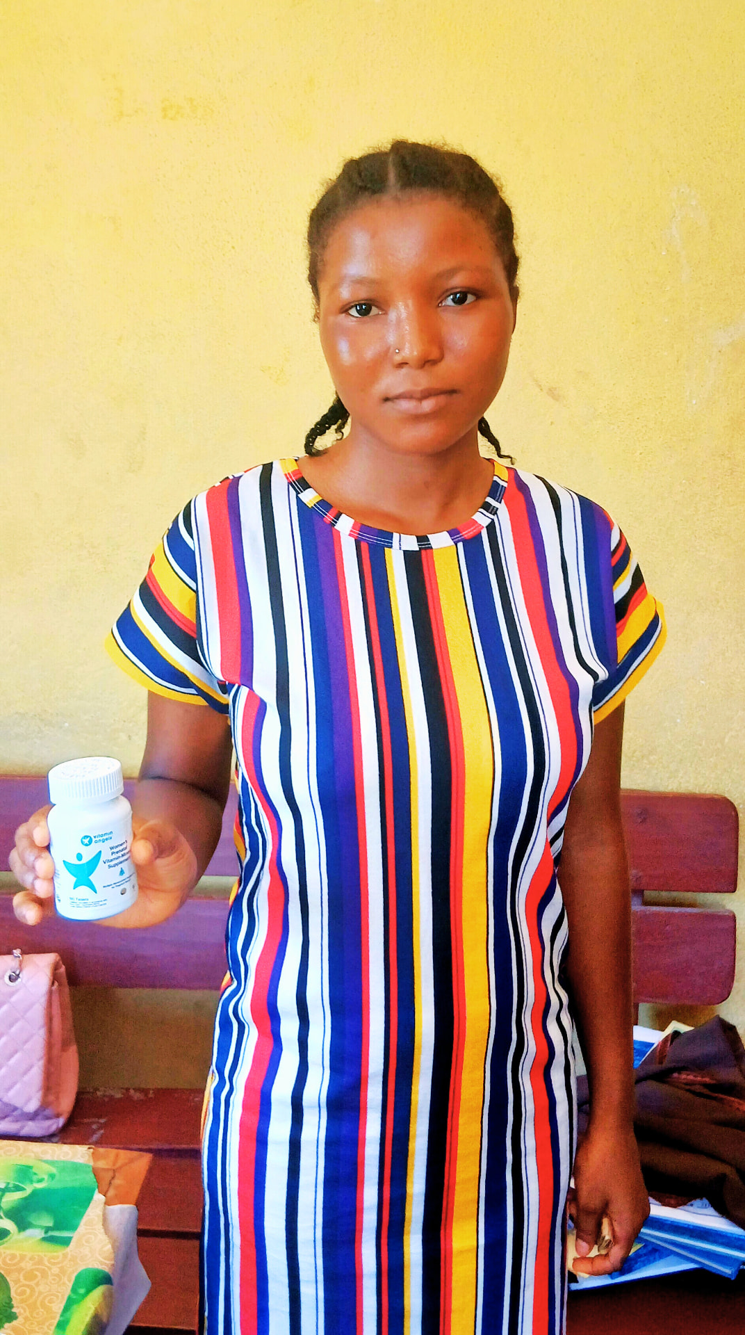 A woman holding a Vitamin Angels bottle inside a health facility