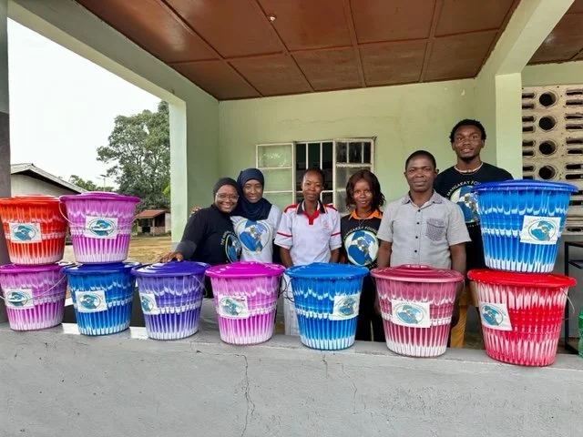 Health workers and TMF team members standing behind rows of colorful birthing buckets