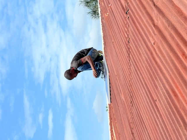 A technician crouching on a red corrugated metal roof while fitting a solar panel