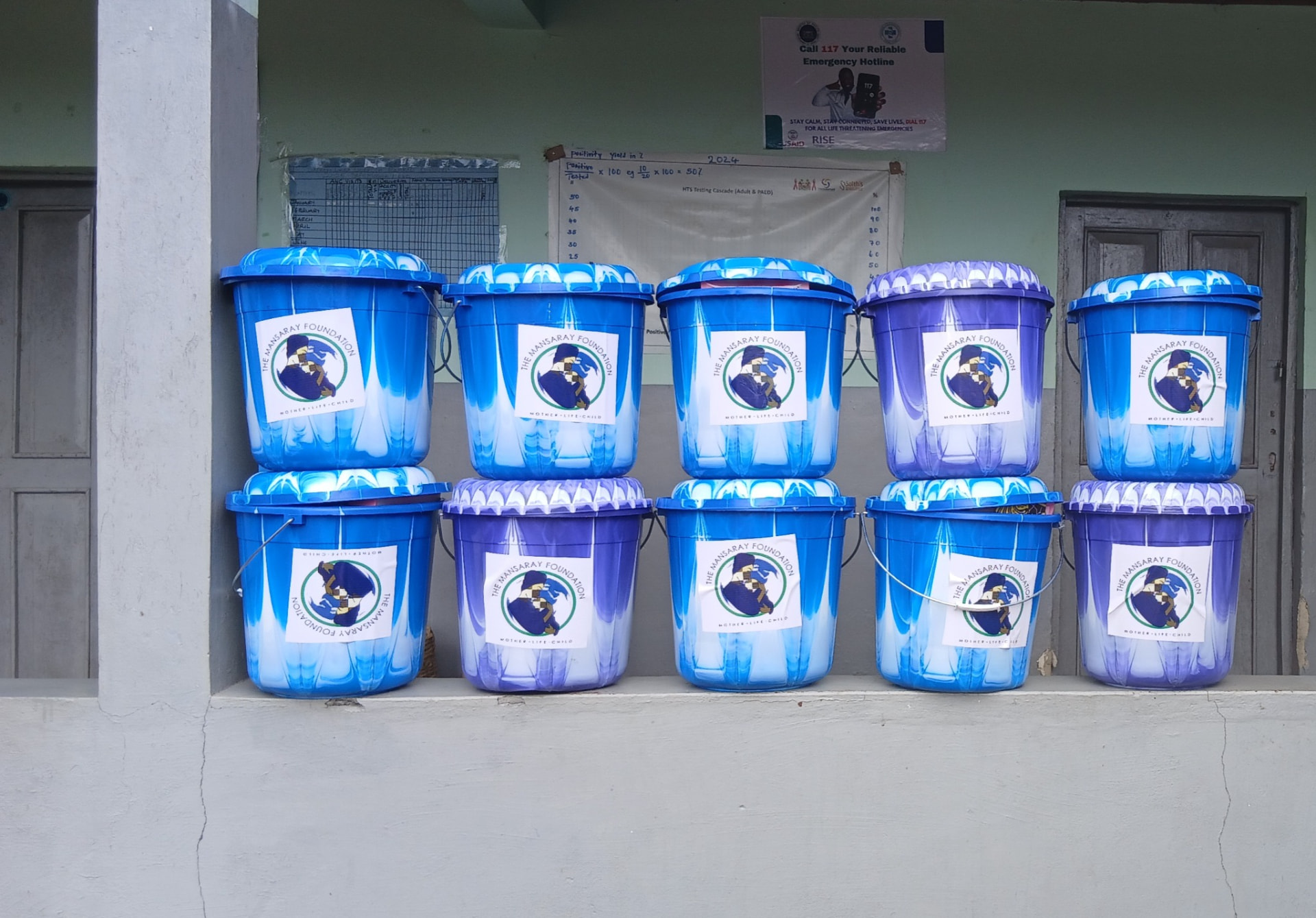 Rows of blue and purple Mansaray Foundation birthing buckets lined up outside a health facility