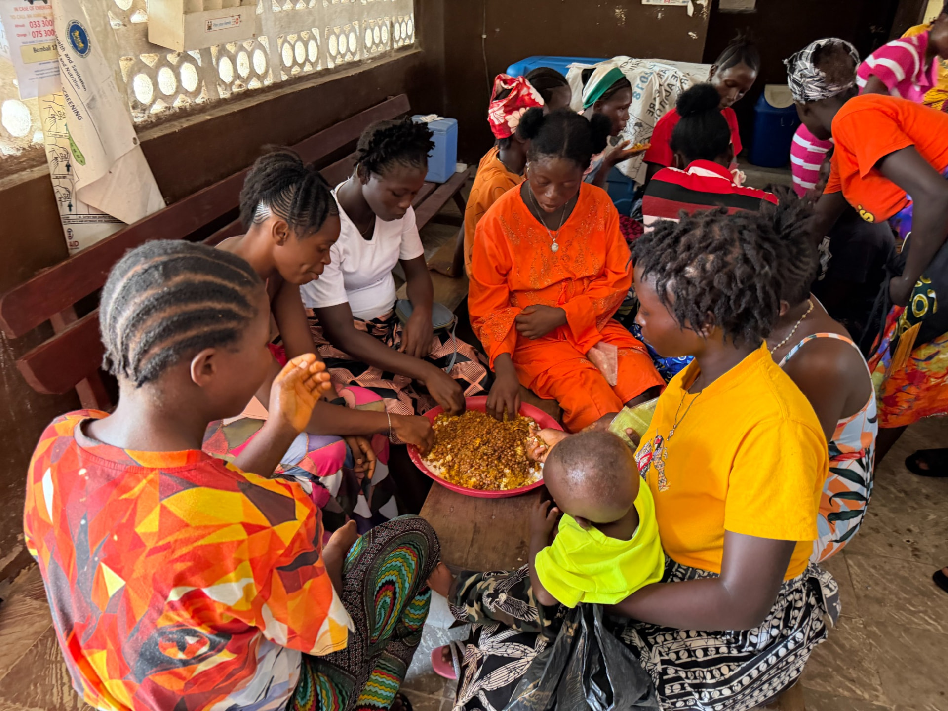 Mothers and children seated around shared bowls of food during a TMF feeding session