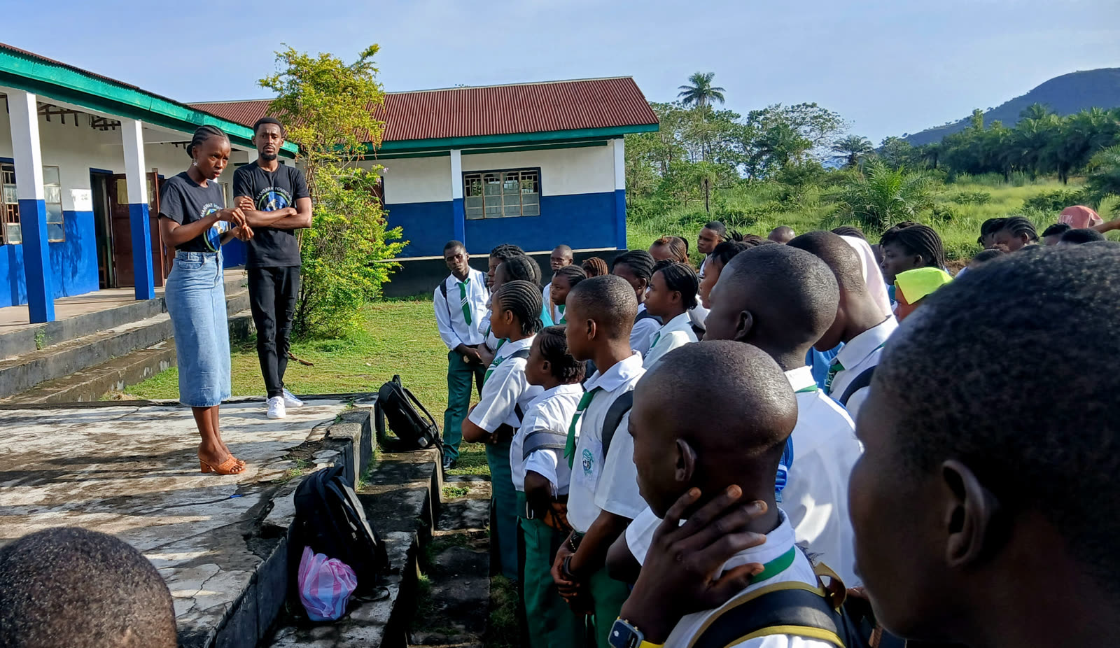 Two TMF team members addressing uniformed students gathered on a school lawn
