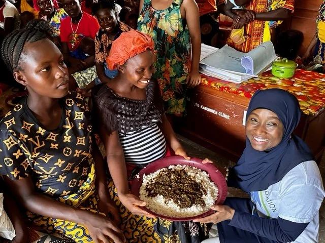 A TMF team member sharing a bowl of food with women during a feeding session