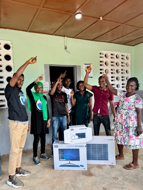 TMF team members and health workers pointing to a new ceiling light, with boxed solar panels and equipment in front of them