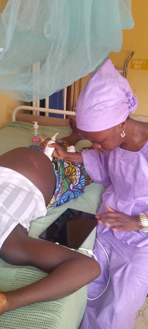 A health worker in a lavender outfit performing an ultrasound scan at a bedside beneath a mosquito net