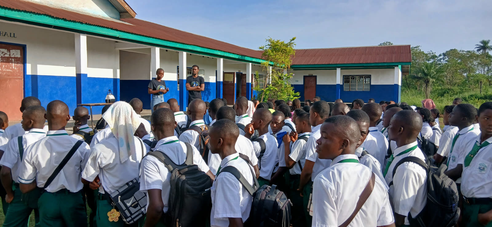 Two TMF team members speaking with a large group of uniformed students outside a school building