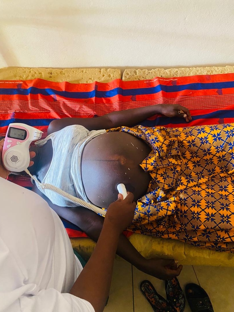 A health worker holding a handheld fetal Doppler against a pregnant woman's abdomen as she lies on a bed