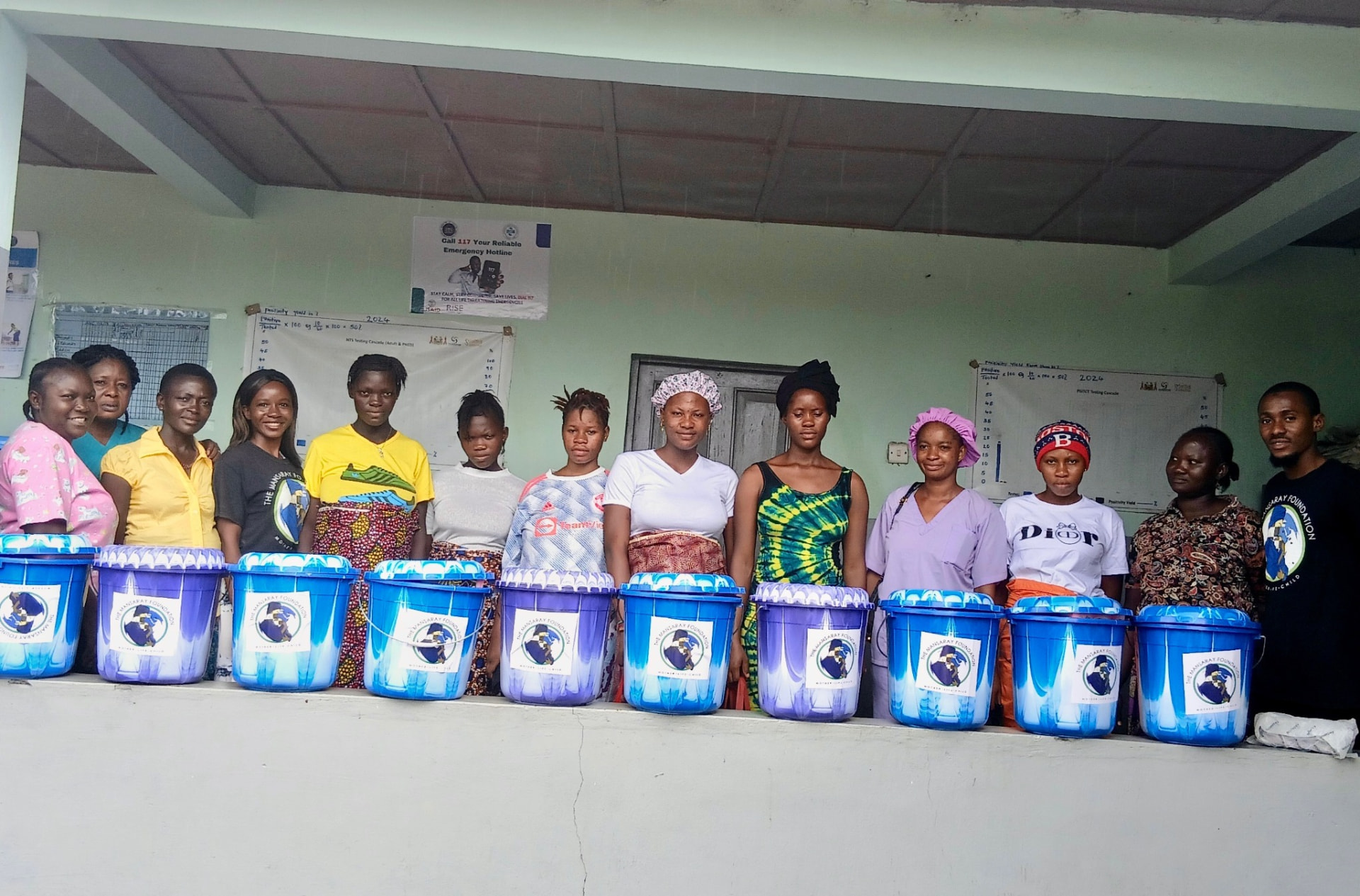 Women standing on a clinic veranda behind a row of Mansaray Foundation birthing buckets