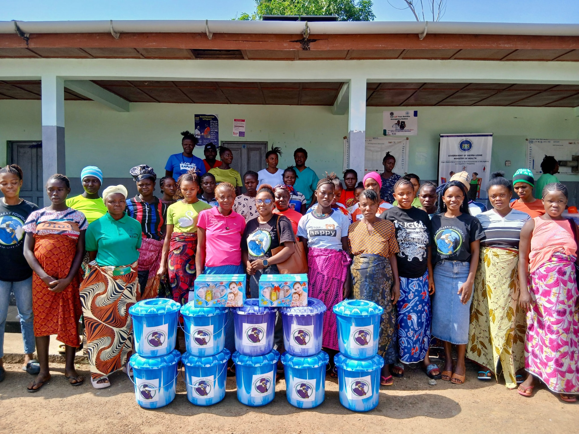 A large group of women and health workers gathered outside a clinic with stacked birthing buckets