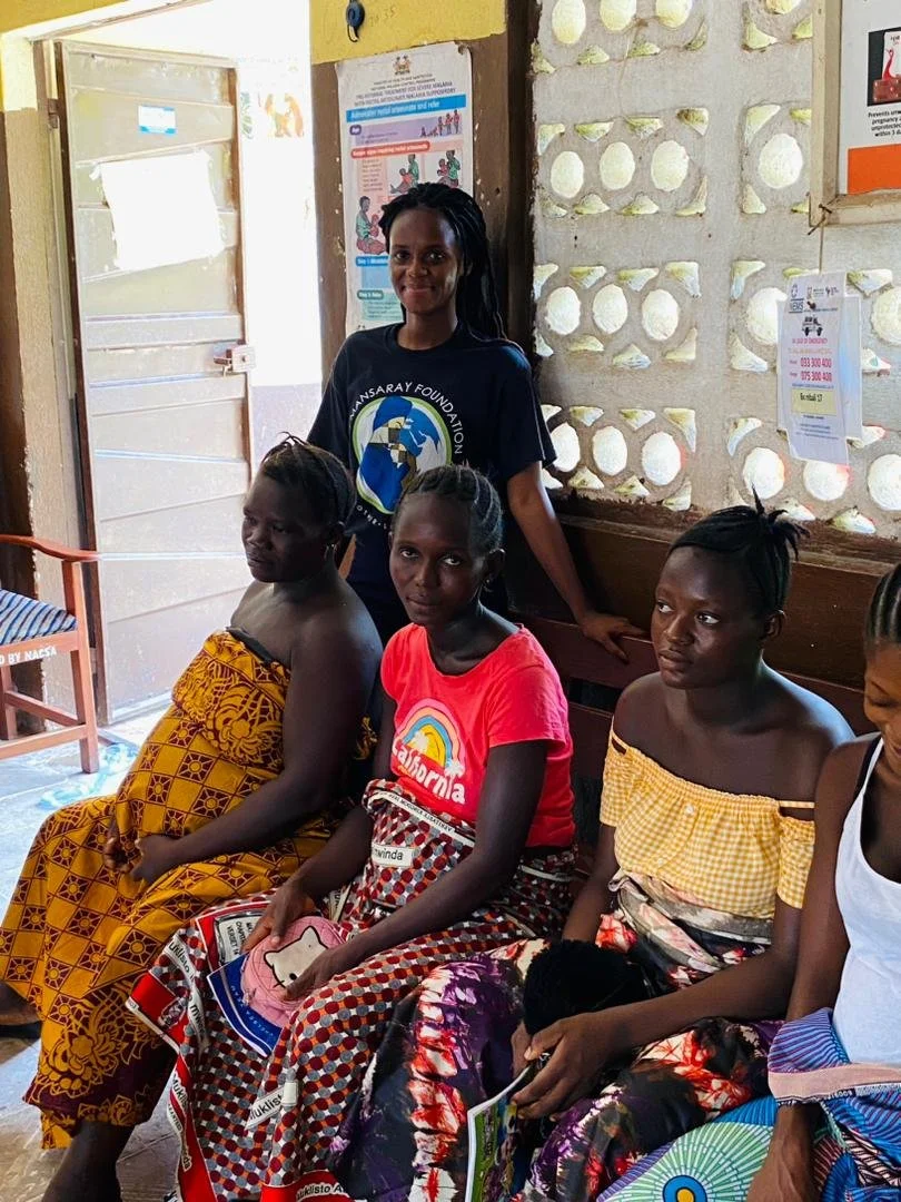 Women seated on a bench inside a clinic with a TMF team member standing behind them