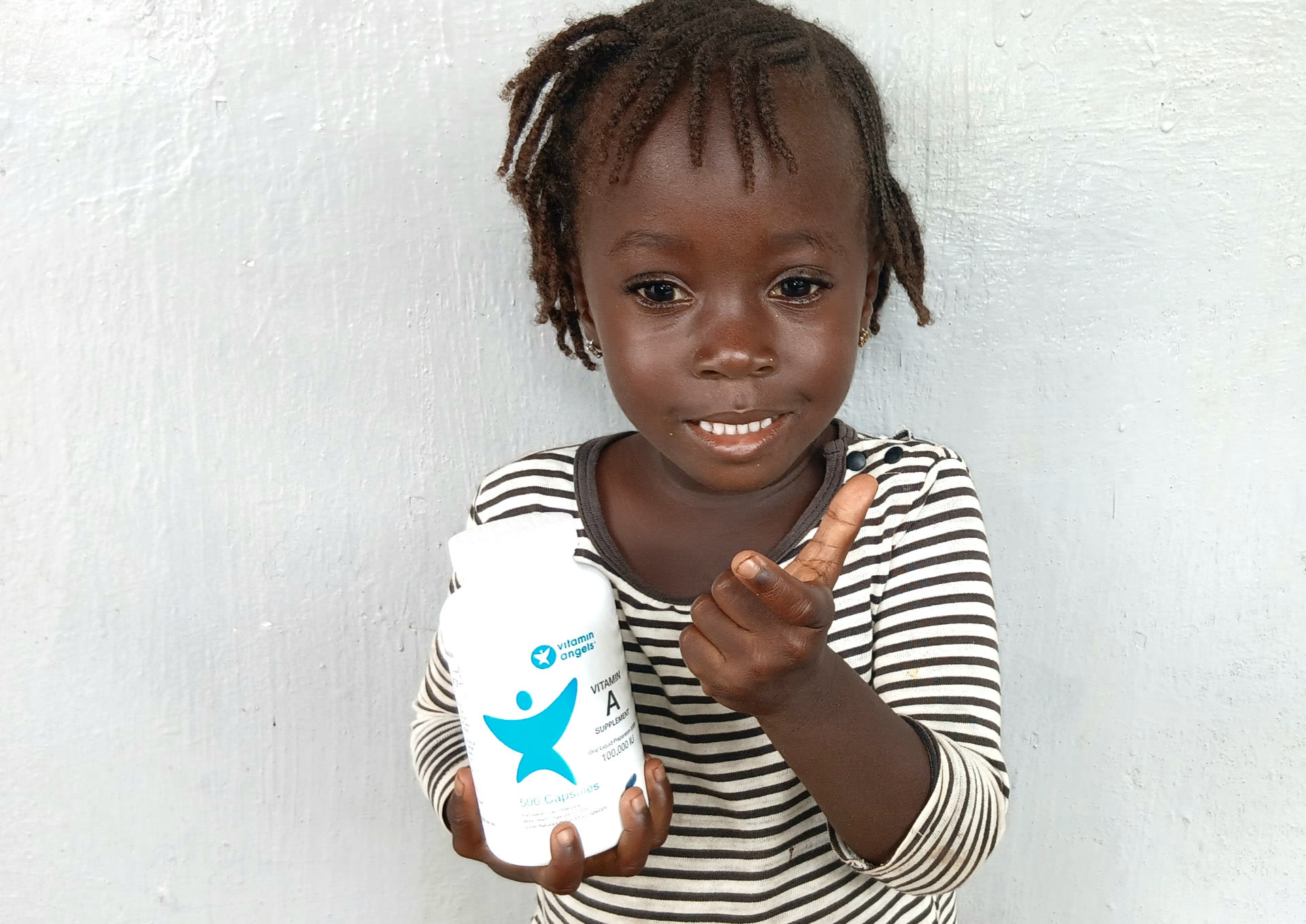 A smiling young child holding a Vitamin Angels bottle
